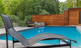 Pool with waterfall treatment, lounge chair, fencing surrounded by great trees